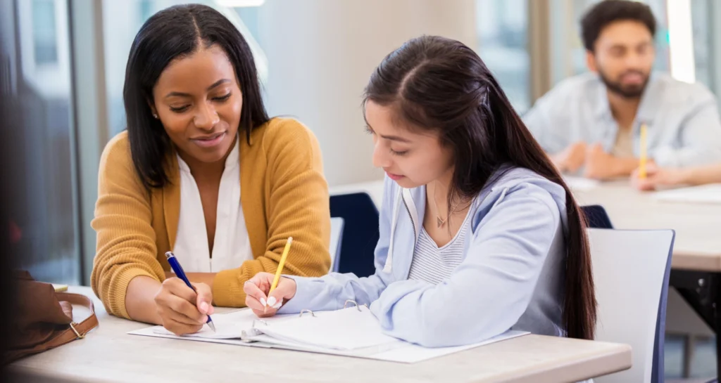 Private tutor explaining written feedback to a student. Secondary school student completing written exam practice